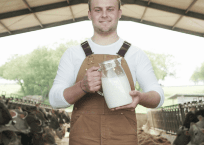 Farmer holding milk with cows in stalls behind him